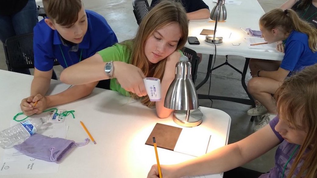 Students measuring the temperature of two different pieces of foam under a heat lamp with a scan thermometer